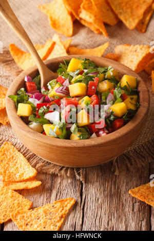Mexikanisches Essen: Salsa mit Mangos, Paprika, Koriander und Zwiebeln hautnah in einer Schüssel und Nachos auf dem Tisch. vertikale Stockfoto