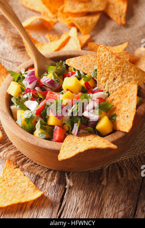 Salsa mit Mangos, Paprika, Koriander und Zwiebeln in einer Schüssel und Nachos hautnah. vertikale Stockfoto