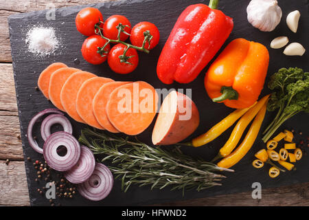 Pflanzliche Inhaltsstoffe: Süßkartoffeln, Paprika, Tomaten, Zwiebeln, Knoblauch, Rosmarin und Gewürze Nahaufnahme auf einer Schiefertafel Tafel. horizontale Ansicht von oben Stockfoto