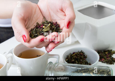 Getrocknete Grüntee in Frauenhand über weißen Tisch mit verschiedenen Arten von Kräutern Stockfoto