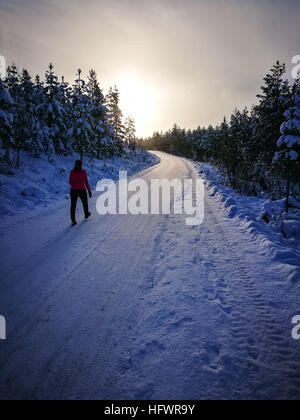 Frau zu Fuß in Sonnenuntergang im Winter auf verschneiten Straßen. Lange Schatten. Stockfoto