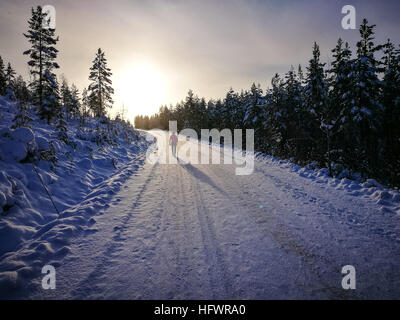 Frau zu Fuß in Sonnenuntergang im Winter auf verschneiten Straßen. Lange Schatten. Stockfoto