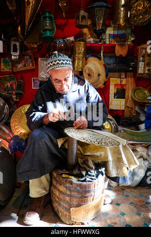 Eine marokkanische Kupfer und Silber-Smith Hämmer Platten im Kettanine Viertel der Medina von Fes, Marokko, umgeben von seiner Arbeit. Stockfoto