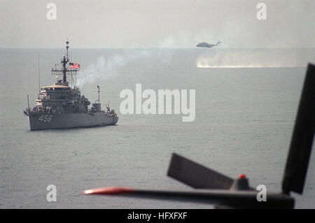 Ein Bogen Blick auf den Hafen des Ozeans Minesweeper USS INFLICIT (MSO 456) vor Anker und ein Hubschrauber Mine Gegenmaßnahmen Staffel 14 (HM 14) RH-53D Sea Stallion Helikopter Praktiken Minenräumung Techniken über den Golf. USS zufügen (MSO-456) und RH-53D im Persischen Golf 1987 Stockfoto