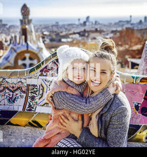 Barcelona-Handschrift. Porträt des Lächelns moderne Mutter und Kind Reisende in Barcelona, Spanien zu umarmen, sitzend auf einer Bank Stockfoto