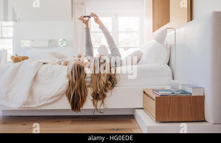 Junge Familien nehmen Selfie mit Smartphone im Bett. Mutter und Tochter am Bett unter Selbstporträt im Schlafzimmer liegen. Stockfoto