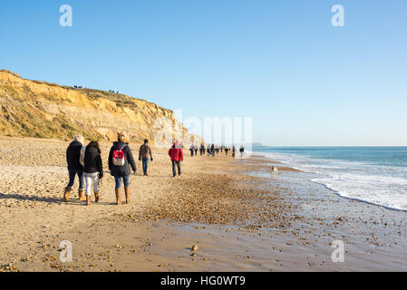 Menschen, die am Strand von Hengistbury Head, Christchurch, Dorset, Großbritannien, bei Wintersonnenwende im Januar spazieren gehen. Stockfoto