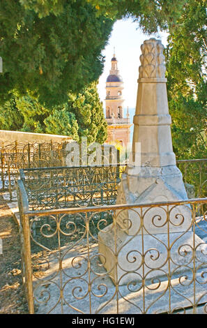 Der Grabstein auf dem Alten Burgberg Friedhof, umgeben von üppigen Bäumen und mit Glockenturm von Saint-Michel Basillica im Hintergrund, Menton, Frankreich Stockfoto