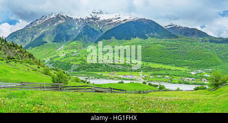 Der Panoramablick auf das Flusstal mit grünen Wiesen und Wäldern auf den Pisten und verschneite Berggipfel, Mestia, obere Swanetien, Georgia. Stockfoto