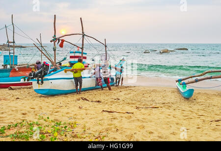 Die Wochentage der srilankischen Fischer, gehen auf das Meer vor dem Sonnenaufgang und zurück zum Hafen bei Sonnenuntergang, Lenkung ihrer schwere Boot in den sand Stockfoto