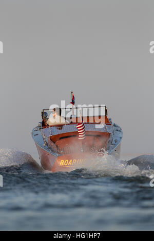 Ein Mann, der in einem antiken, hölzernen Schnellboot davonfährt. Stockfoto