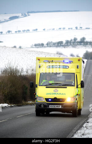 Krankenwagen auf einer Landstraße, umgeben von Schnee im Winter. Stockfoto