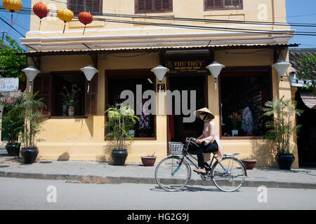 Frau auf dem Fahrrad außerhalb Schneiderei Hoi An Vietnam Stockfoto