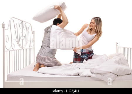 Junger Mann und Frau, die eine Kissen kämpfen auf einem Bett isoliert auf weißem Hintergrund Stockfoto