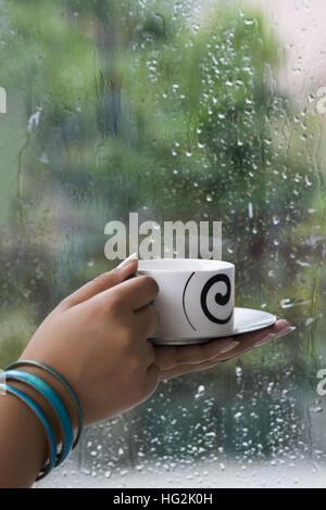 In der Nähe der Cup in der Frau die Hand vor der Regenzeit Fenster Glas Stockfoto