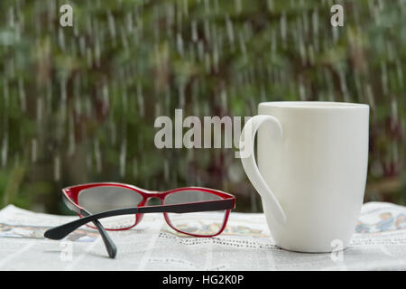 Lesebrillen und Kaffeetasse auf Zeitung regnerischen Fenster Glas Stockfoto