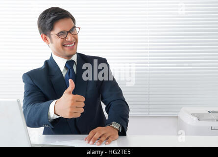 Junge Mann in fröhliche Stimmung mit Daumen nach oben unterzeichnen und winking Eye im Büro Stockfoto