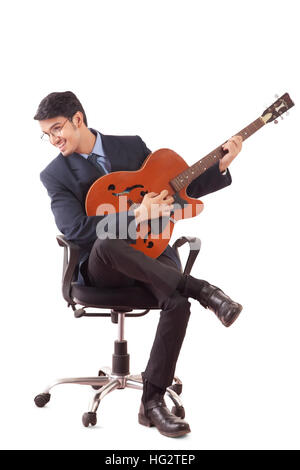 Lächelnden jungen Mann in formelle Kleidung, Gitarre zu spielen, sitzen auf den drehstuhl vor weißem Hintergrund Stockfoto