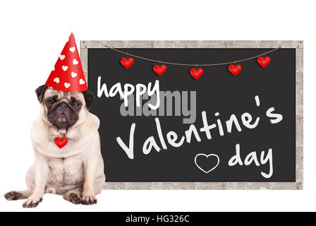 mürrisch süße Mops Welpen Hund trägt Partyhut mit Herzen, sitzt neben Tafel Schild mit Text happy Valentinstag, auf weißem Hintergrund Stockfoto