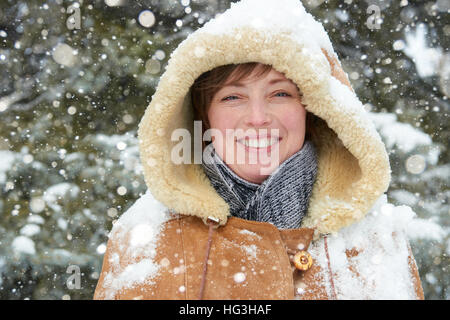 schöne Frau Porträt über Winter im Freien, verschneite Tannen im Wald, lange rote Haare, trägt einen Lammfell-Mantel Stockfoto
