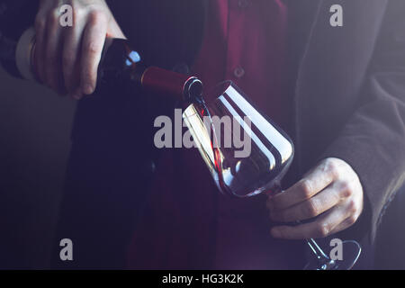 Horizontale Nahaufnahme von kaukasischen Mann im schwarzen Anzug und Hemd strömenden Rotwein in ein hohes Glas in einer bar Stockfoto