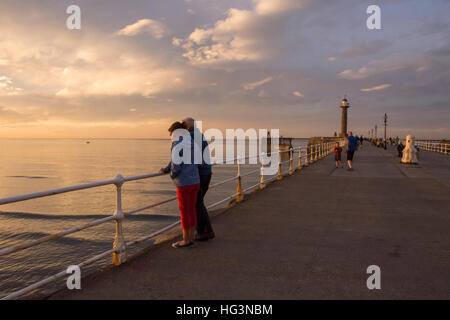 Bunter Himmel und Meer bei Sonnenuntergang genossen an einem Sommerabend von den Leuten auf der West Pier, Whitby, North Yorkshire, England. Stockfoto