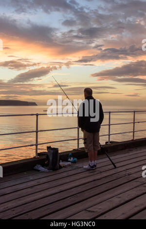Malerische Whitby & gegen die drastischen, farbenfrohen sonnenuntergang himmel Silhouette, Mann (Angler) ist der Seefischerei von West Pier - North Yorkshire, England, UK. Stockfoto