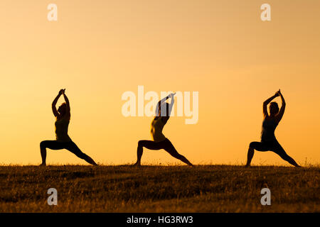 Drei Mädchen üben Yoga bei Sonnenuntergang. Stockfoto