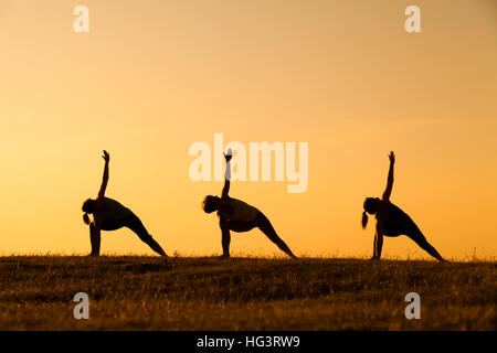 Drei Mädchen üben Yoga bei Sonnenuntergang. Stockfoto