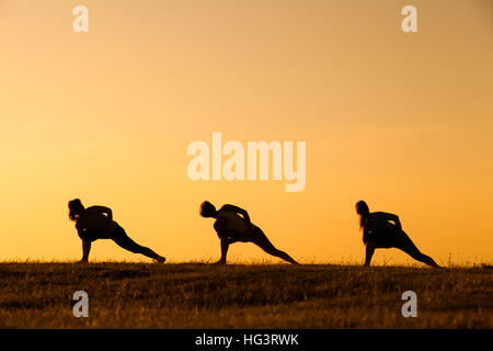 Drei Mädchen üben Yoga bei Sonnenuntergang. Stockfoto