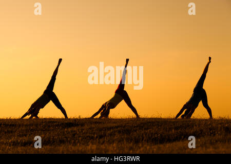 Drei Mädchen üben Yoga bei Sonnenuntergang. Stockfoto