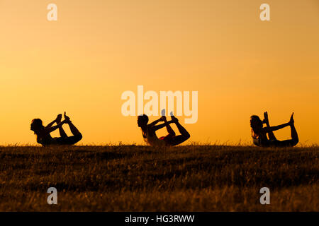 Drei Mädchen üben Yoga bei Sonnenuntergang. Stockfoto