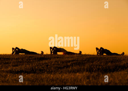 Drei Mädchen üben Yoga bei Sonnenuntergang. Stockfoto