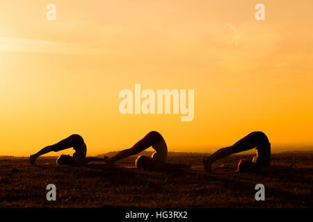 Drei Mädchen üben Yoga bei Sonnenuntergang. Stockfoto