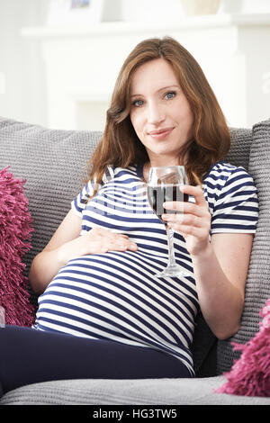 Schwangere Frau trinken Rotwein zu Hause Stockfoto