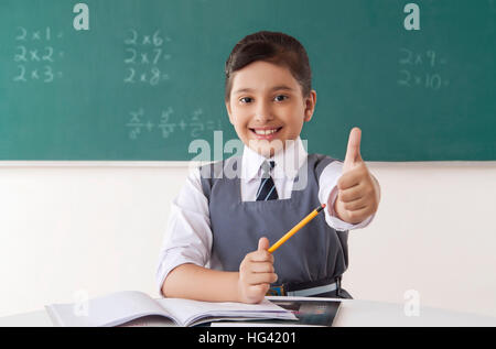 Lächelnde Mädchen zeigen Daumen hoch in einem Klassenzimmer Stockfoto