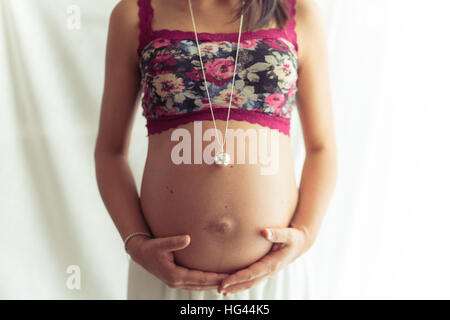 Schwangere Frau mit Blume oben und Halskette mit Anhänger. Stockfoto