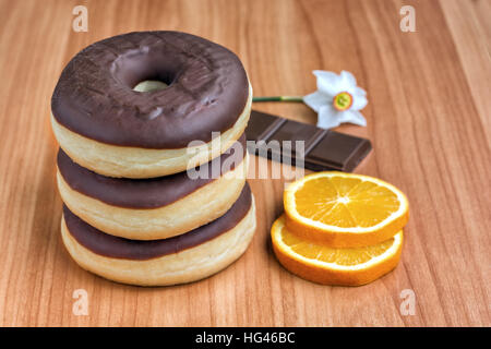 Drei Donuts mit dunklen Schoko-Orangen Scheiben auf einem Holzsockel Stockfoto