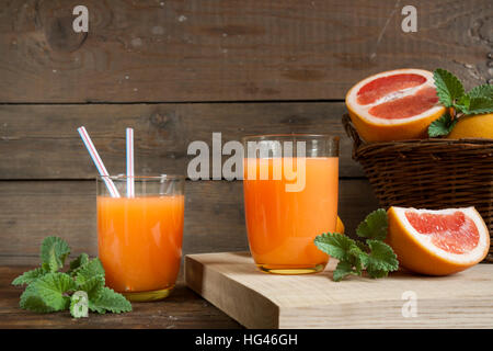 Natürliche und frische Grapefruit-Saft im Glas mit frisch geernteten Grapefruit im Korb auf dunklem Holz Stockfoto