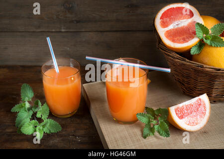 Natürliche und frische Grapefruit-Saft im Glas mit frisch geernteten Grapefruit im Korb auf dunklem Holz Stockfoto