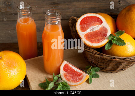 Natürliche und frische Grapefruit-Saft in kleinen Flaschen mit frisch geernteten Grapefruit im Korb auf dunklem Holz Stockfoto