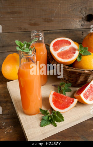 Natürliche und frische Grapefruit-Saft in kleinen Flaschen mit frisch geernteten Grapefruit im Korb auf dunklem Holz Stockfoto