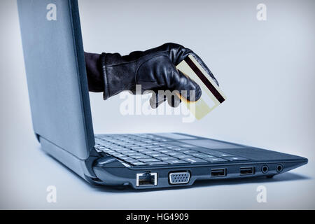 Eine behandschuhte Hand erreichen durch einen Laptop mit Debit- oder Kreditkarte, bedeutet ein Cybercrime oder Internet Diebstahl. Stockfoto
