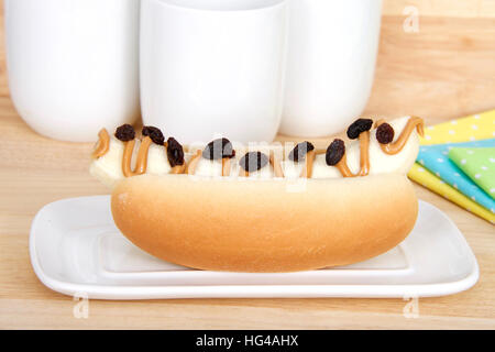 Banane mit Erdnussbutter und Rosinen an der Spitze in einem Hot-Dog-Brötchen auf einem weißen rechteckigen Platte, gelb, blau, grün Polka Dot Servietten und Becher in staatlich Stockfoto