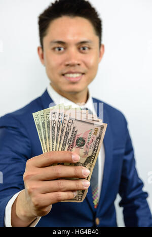 Ein lächelnder asiatischen Mann im blauen Anzug verteilt Geld in der Hand und ausstrecken. Ausdruck der Zahlung per Nachnahme. Formalen Geschäft. Stockfoto