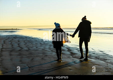 Ein junges Paar in Liebe Hand in Hand am Strand bei Sonnenuntergang. Stockfoto