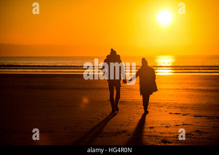 Ein junges Paar in Liebe Hand in Hand am Strand bei Sonnenuntergang. Stockfoto