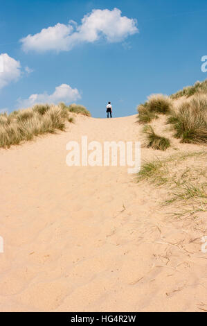 Junge Frau, die in der Frühlingssonne auf einer Sanddüne in Burnham Overy Staitthe, Norfolk, England, Großbritannien, steht. Stockfoto