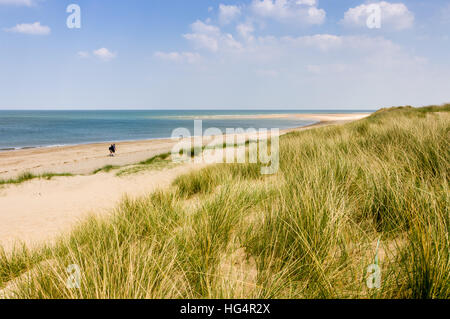 Zwei Personen mit Rucksäcken gehen an einem sonnigen Frühlingstag einen Sandstrand entlang in Burnham Overy Staitthe, Norfolk, England, Großbritannien. Stockfoto