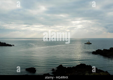 Mündung des Fluss Fowey in den Ärmelkanal bei Sonnenuntergang. Ein Schlepper segelt in einem Frachtschiff zum Hafen bringen. Stockfoto